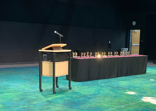 The stage for the Department Awards hosted inside of the Black Box Theatre, featuring a stand with a microphone and a table with all of the awards.